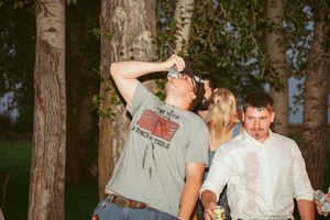 Joyful group celebrates during outdoor wedding reception amid tall trees and natural lighting.