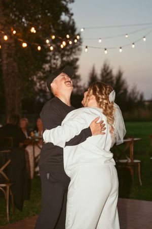 A couple shares romantic dances under glowing string lights during a twilight outdoor party.