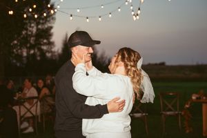 A couple shares their first dance under string lights at an outdoor evening wedding reception.