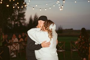 Couple dancing outdoors at sunset while string lights twinkle overhead at an elegant countryside wedding reception.