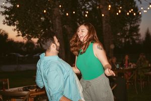 A couple dances together at an outdoor evening event with string lights glowing in the background.