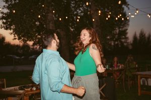 A pair sharing a joyful dance moment outdoors under festive string lights at dusk.
