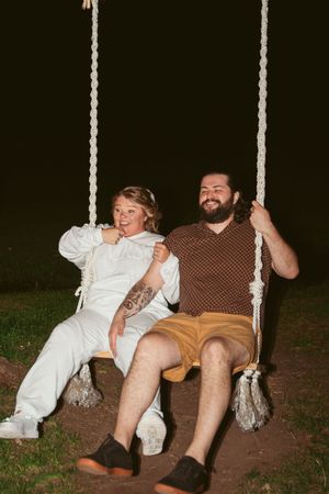 Two people enjoying a playful moment on a rustic rope swing at night.