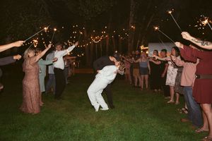 Wedding guests create a sparkler tunnel on a dark lawn as people dance and celebrate at an outdoor reception.