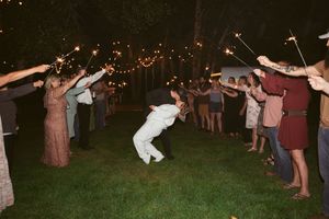 Wedding guests form a sparkler tunnel exit while a celebrating figure dances through in the nighttime.
