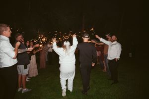 Wedding party celebrates at night outdoors with sparklers illuminating the joyful moment as couple walks through.
