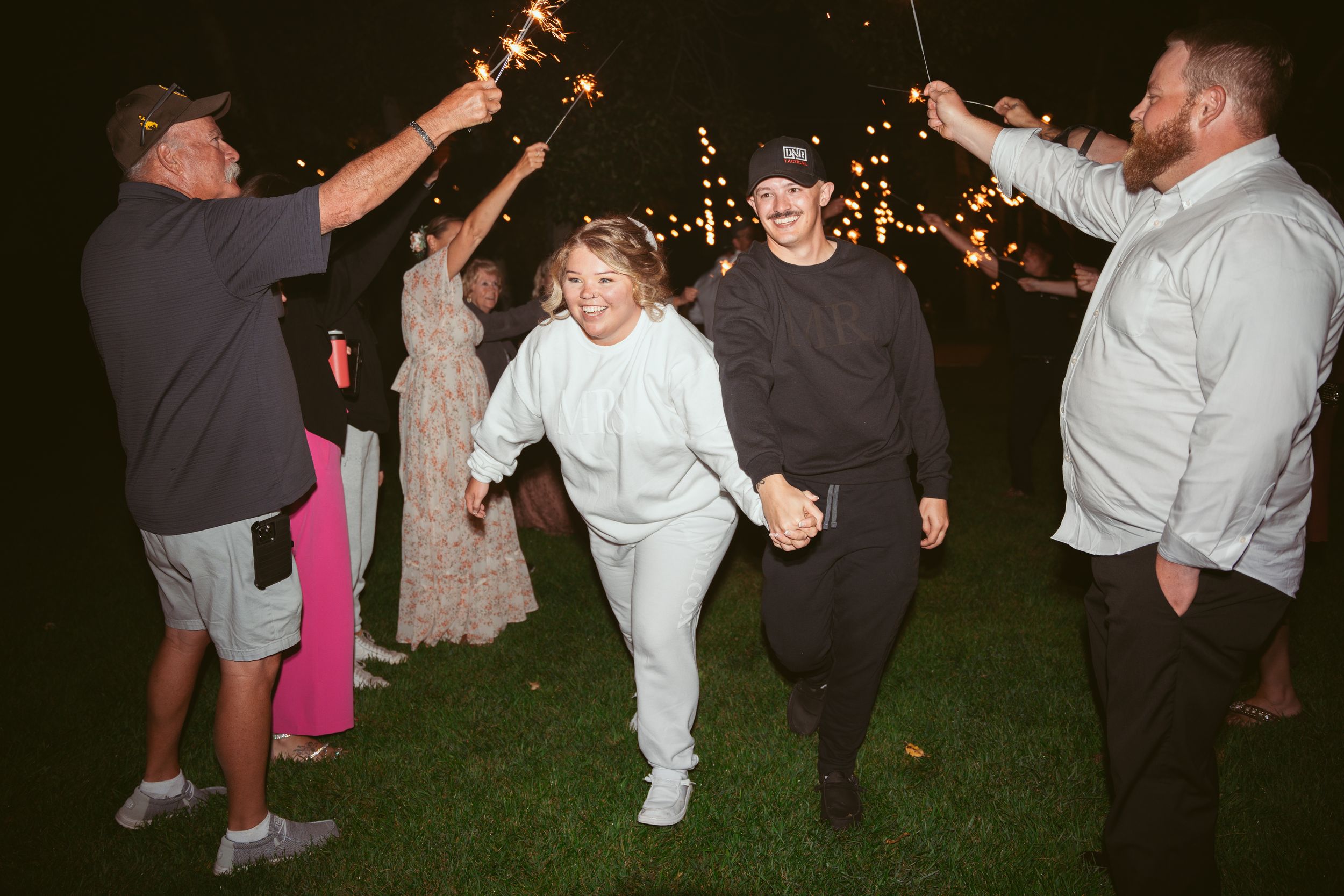 Wedding guests form a tunnel of sparklers during an outdoor evening celebration.