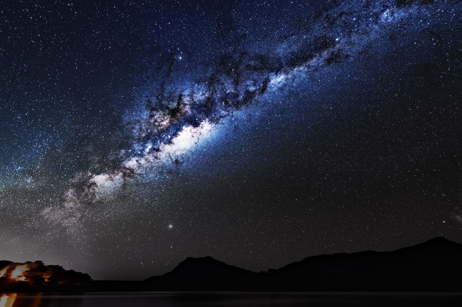 Milky Way galaxy band stretching across dark night sky over mountain landscape.
