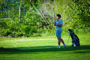 A golfer takes a swing on a lush green course while surrounded by vibrant summer foliage.