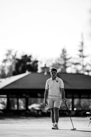 A black and white image shows a golfer on a putting green concentrating on their shot at dusk.
