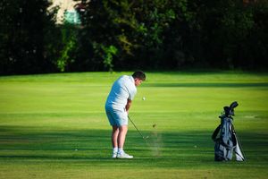 Golfer on a lush green course follows through their swing while practicing putting technique near golf bag at dusk.