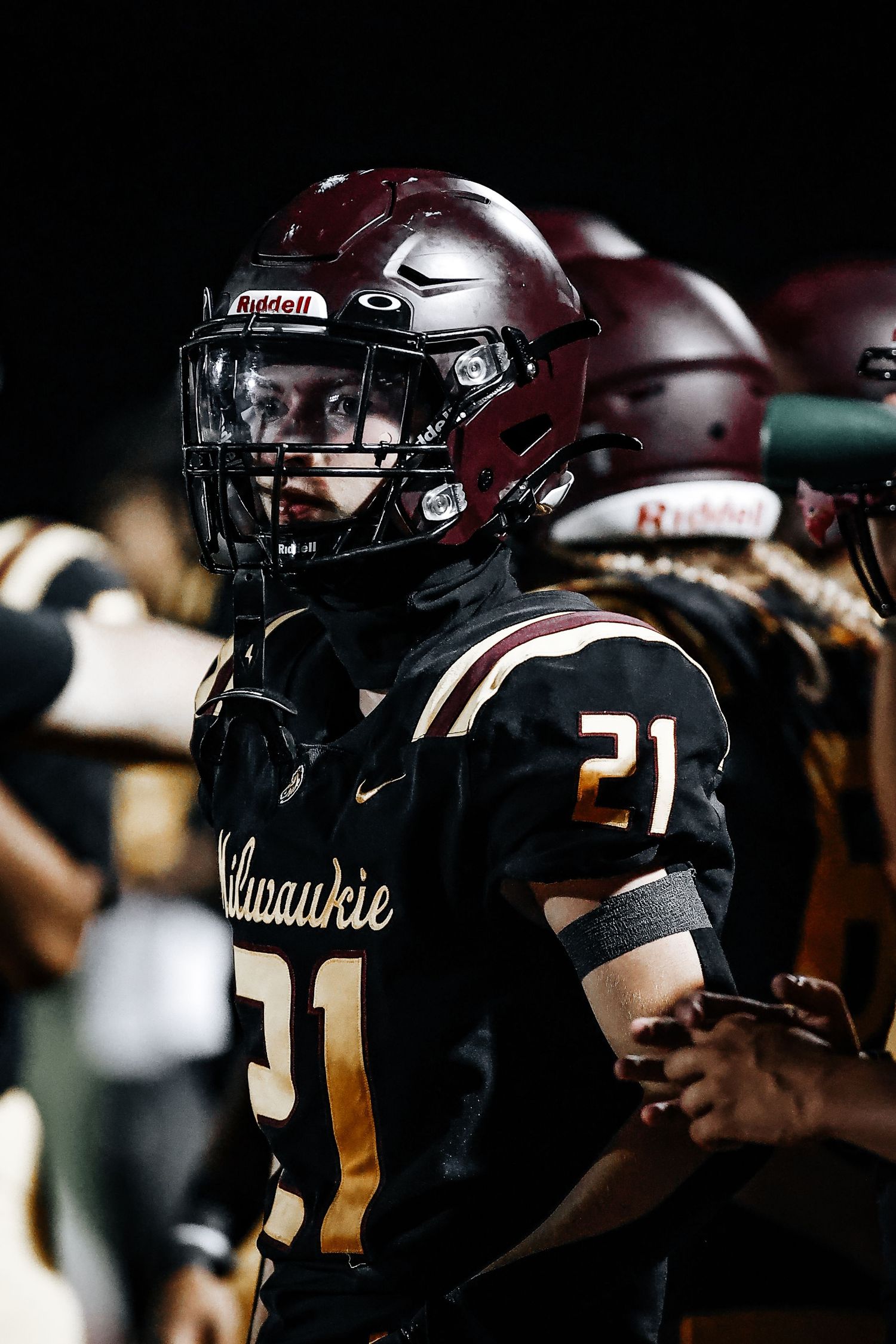 Football player wearing maroon helmet and black Valparaiso jersey number 21 stands on field during night game.