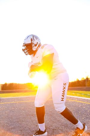 Football player silhouetted against brilliant sunset in white uniform while practicing on field during golden hour.