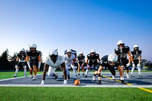 Football team lined up in formation on field during practice with bright blue sky in background.