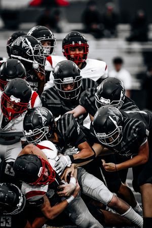 A football team in black uniforms tackles opponents in red jerseys during an intense defensive play.