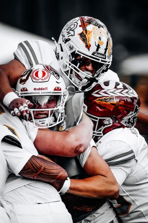 Three football players in white uniforms tackle each other during an intense game action shot.