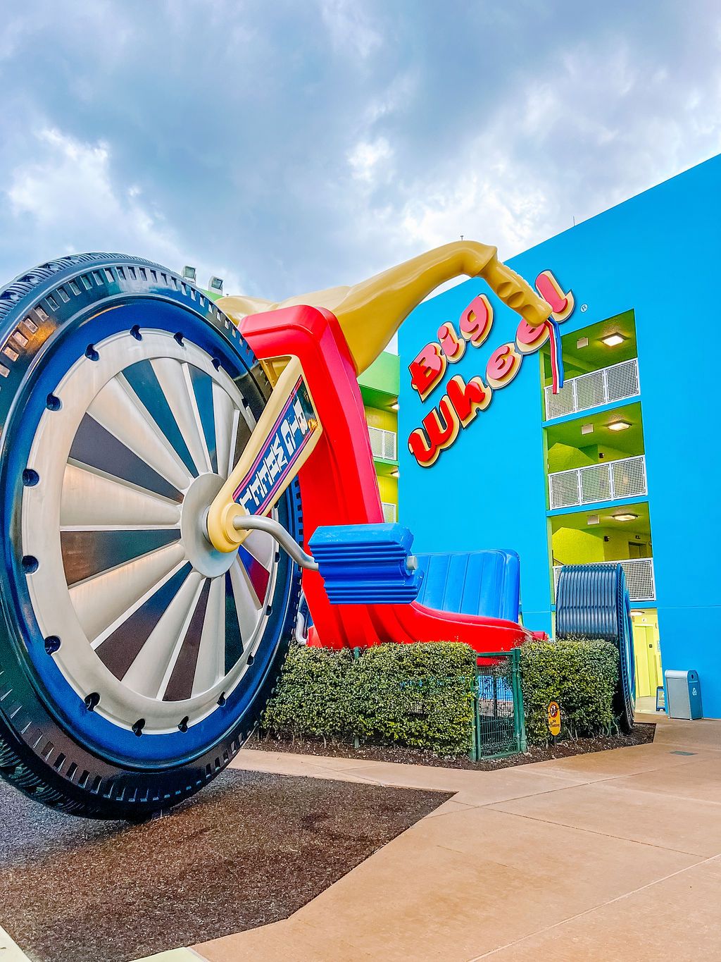 Giant decorative Big Wheel toy installation against bright blue wall at Disney resort.