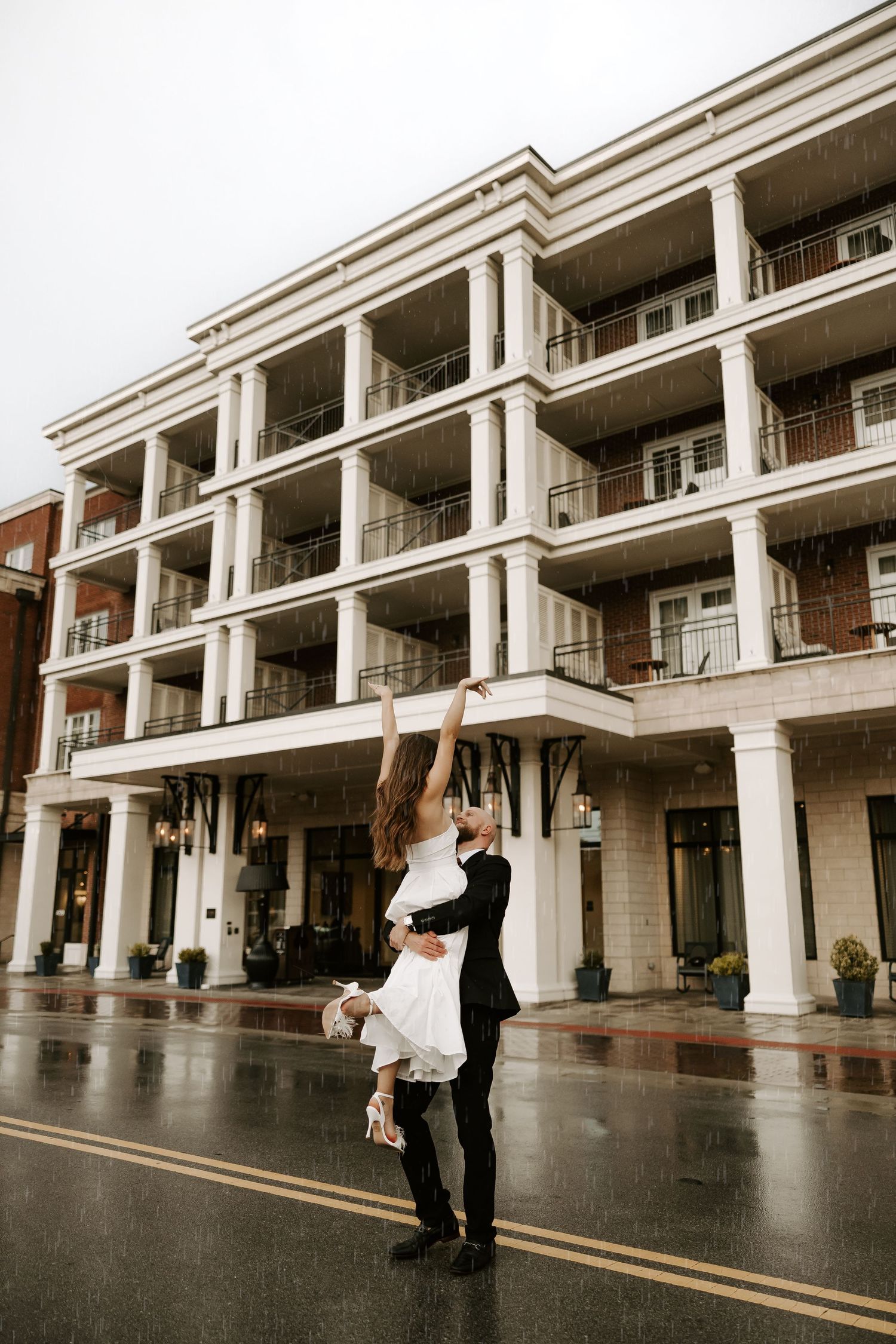 A romantic dance lift in the rain outside a columned building with white architecture.