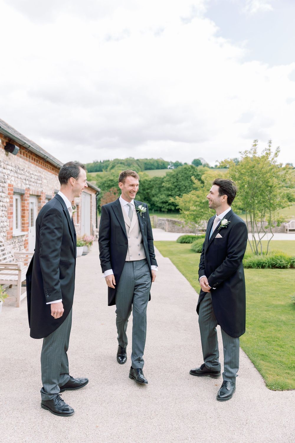 Groomsmen in formal attire gathering outside a brick venue before the wedding ceremony.