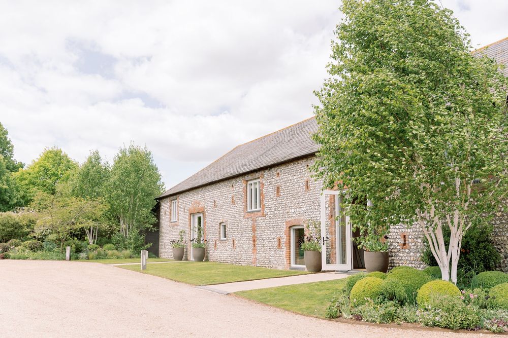 A rustic stone barn wedding venue with manicured gardens and trees.