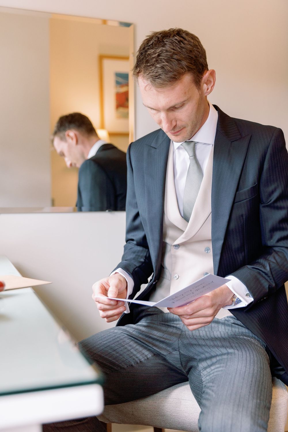 Person in formal attire writing in a notebook while seated on a couch.