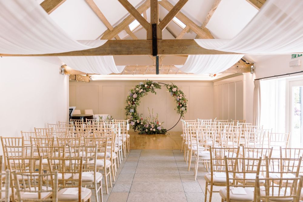 Modern white wedding venue with wooden beams and rows of elegant chiavari chairs set up for a ceremony.