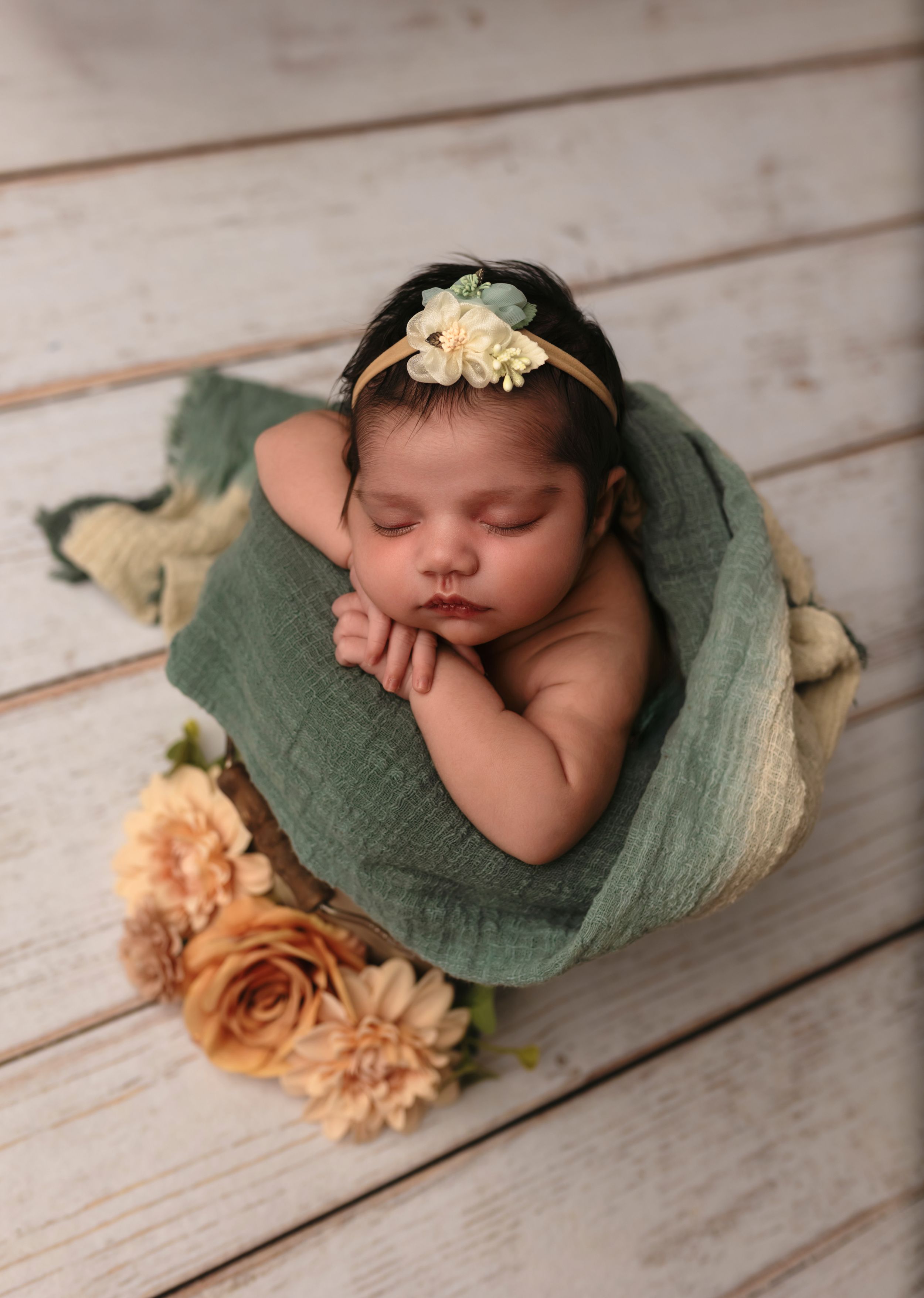 Newborn girl sleeping in a basket with a turquoise blanket and floral headband during a studio session in Charlottesville, Virginia.
