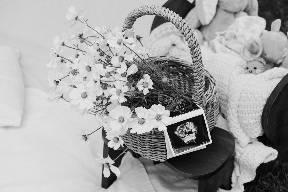 A woman's hands carefully arranging fresh white flowers and foliage into a wicker basket for an elegant floral display.