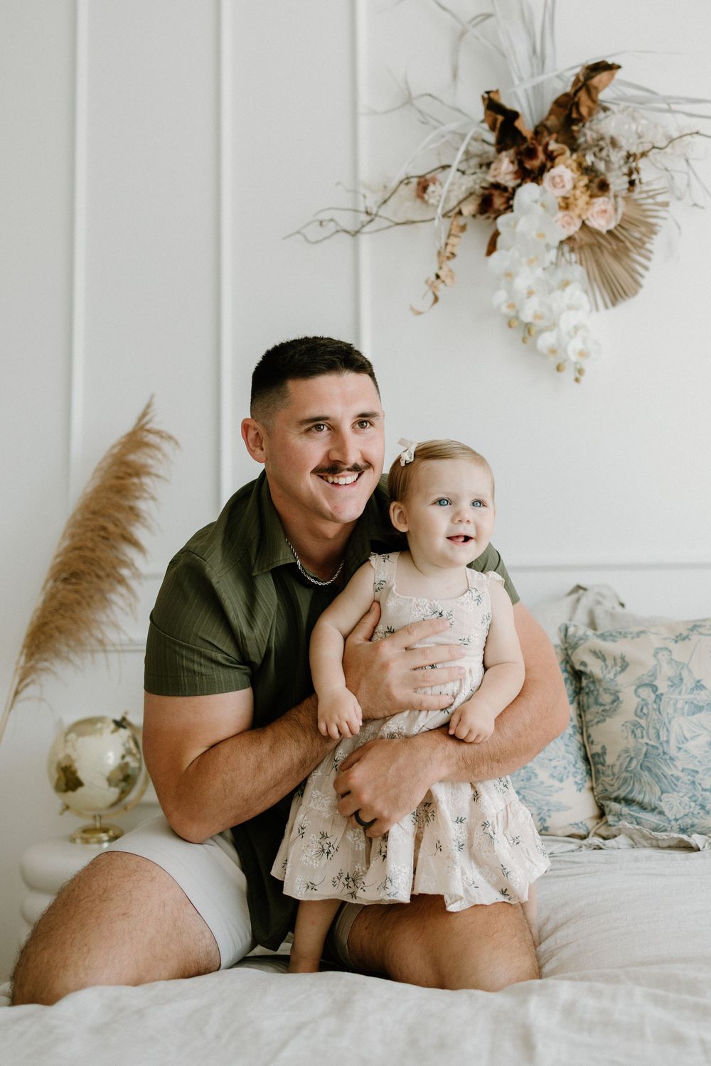 A series of candid moments captured on a white bed with dried floral decor in the background.