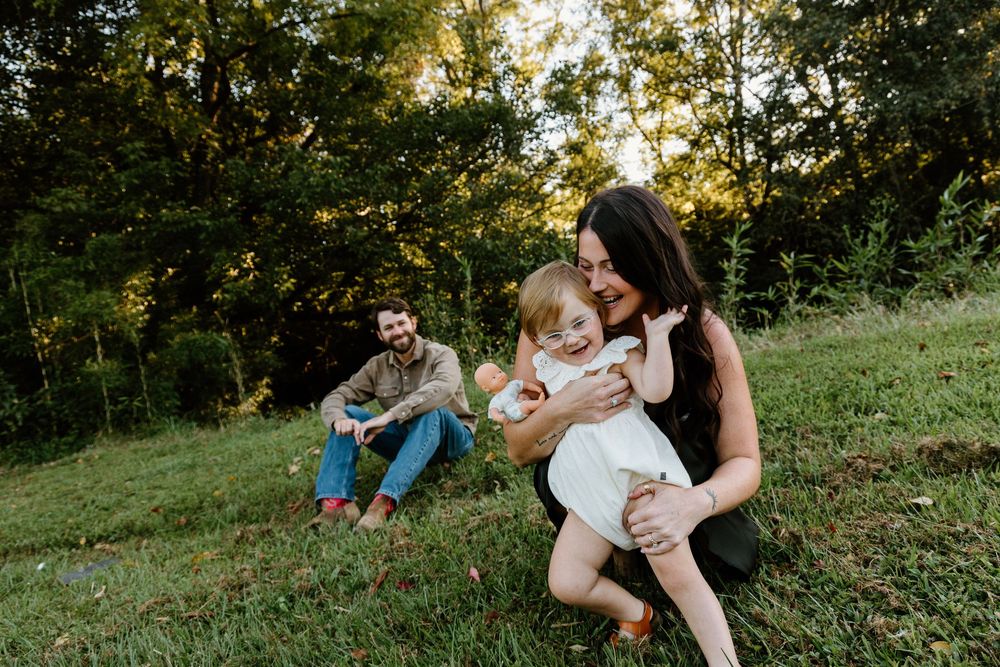 A family shares tender moments together on a grassy hillside during golden hour sunset.