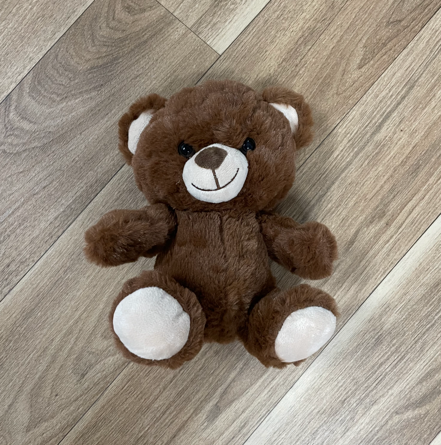 A classic brown teddy bear with white paws and nose sitting on hardwood flooring.