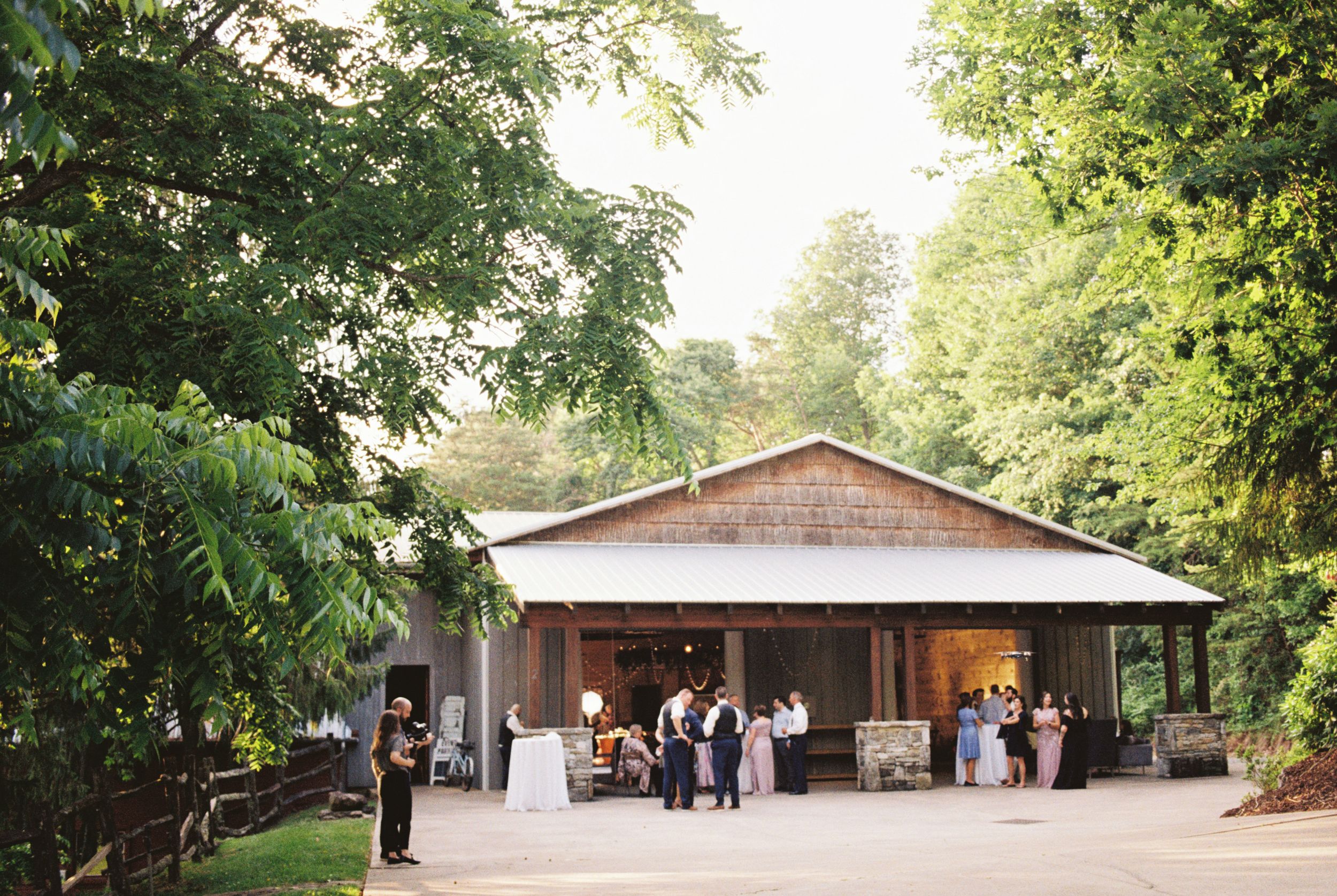 A rustic wooden pavilion venue nestled among lush green trees provides an elegant setting for outdoor gatherings.