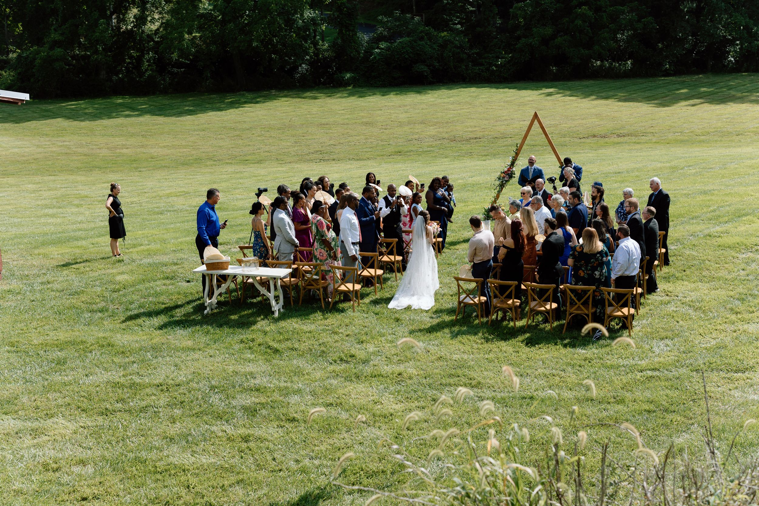 An intimate outdoor wedding ceremony at Honeysuckle Hill wedding venue on a lush green lawn with wooden chairs and a simple wooden arch.