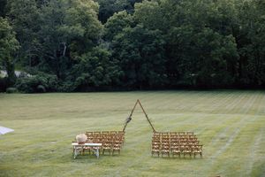 Wooden chairs arranged for an outdoor wedding ceremony on a lush green lawn with forest backdrop.