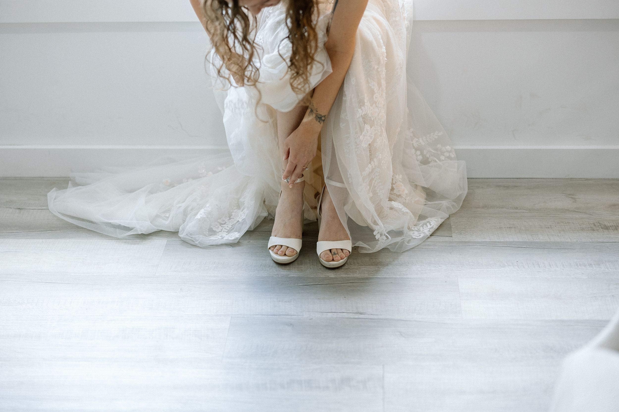 Close-up view of elegant bridal shoes and flowing white wedding dress hem on light neutral floor.