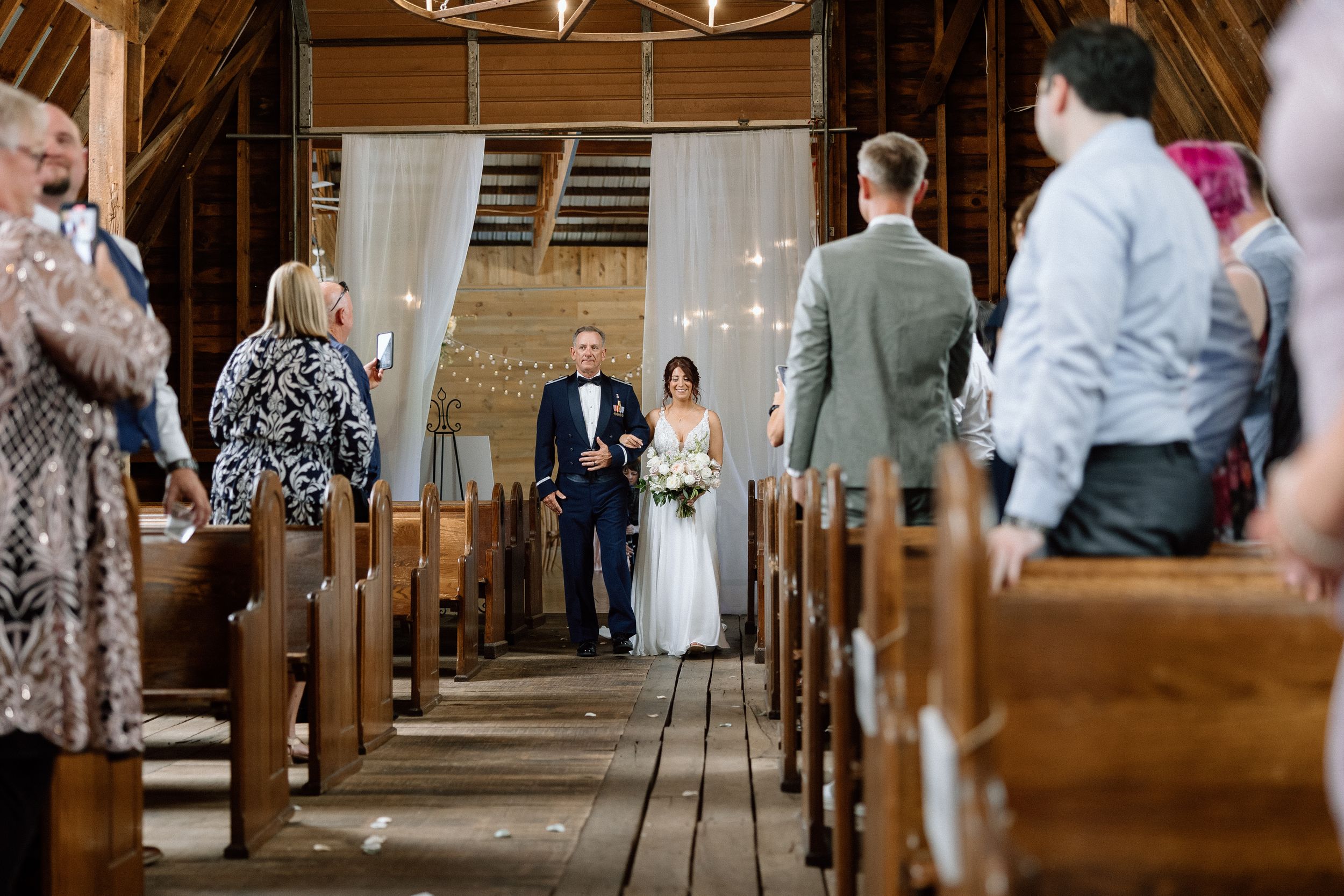Wedding guests seated in pews at a traditional church ceremony with white decor and chandelier lighting in the barn at Honeysuckle Hill.