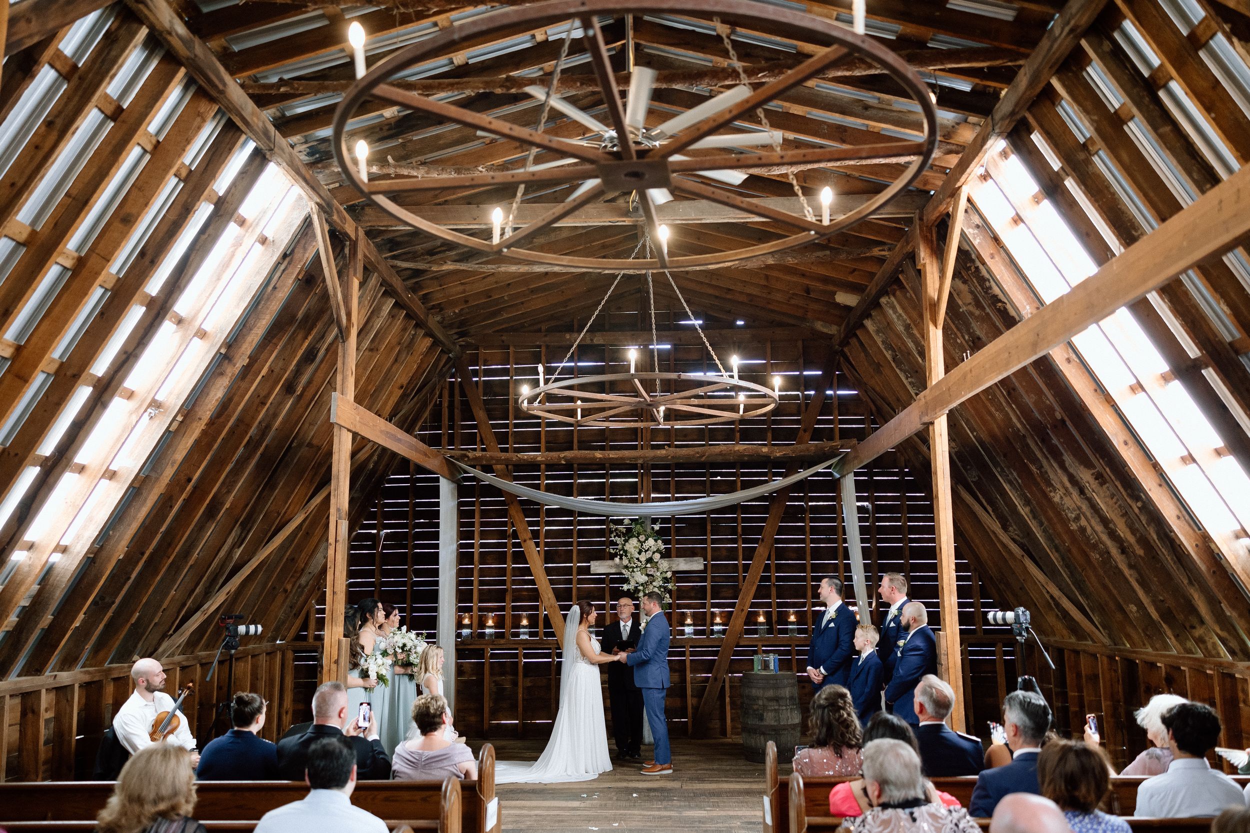 A rustic wooden barn attic space decorated for a wedding ceremony with hanging lights and natural skylights.