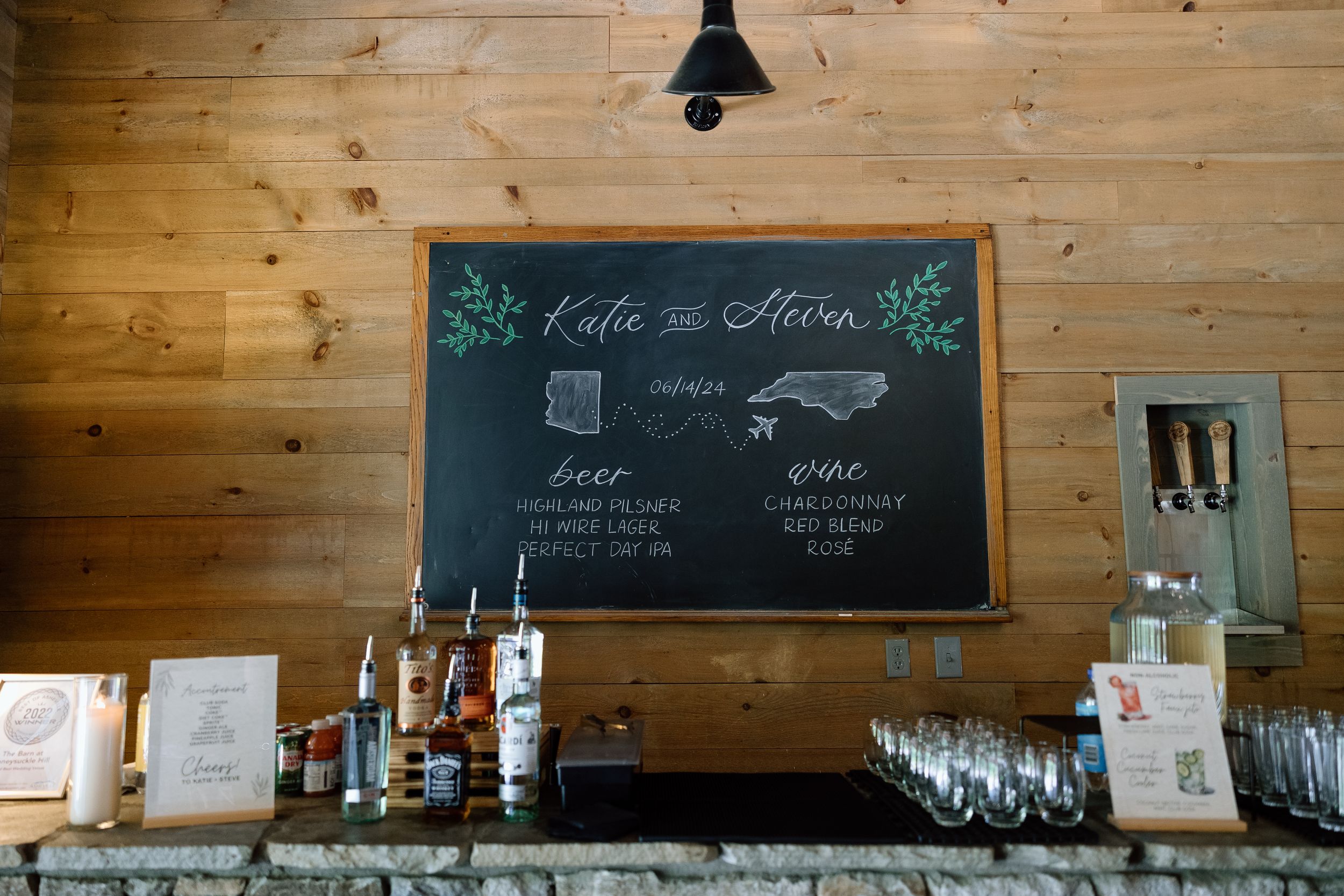 A rustic wooden bar with a chalkboard menu and drink station featuring liquor bottles and glassware.
