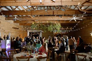 A rustic indoor event venue with string lights, exposed wooden beams, and guests gathered at tables for a celebration.