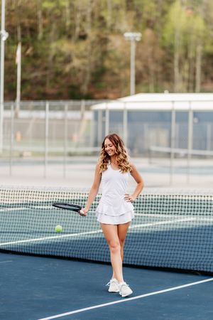 Young woman in white tennis dress holding racket on outdoor court.