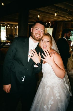 Newlywed couple smiling and showing off wedding rings at rustic barn reception venue.