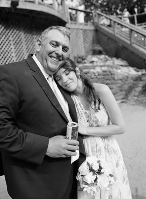 Black and white photo of a smiling man in a suit with a woman leaning on his shoulder holding a bouquet.