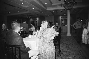 A wedding reception scene showing guests dining at decorated tables in an elegant ballroom.
