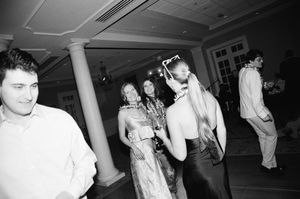 Black and white photograph of guests dancing at an indoor reception with white pillars.