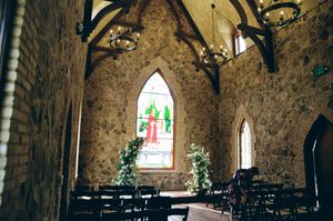 Stone chapel interior with stained glass windows, Gothic arches, and wooden chairs arranged in rows for seating.
