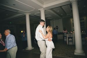 Guests dancing at wedding reception in elegant ballroom with classic white columns and dark floors.