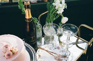Elegant table setting with champagne bottle, crystal glasses, and white flowers in glass vases on a mirrored tray.