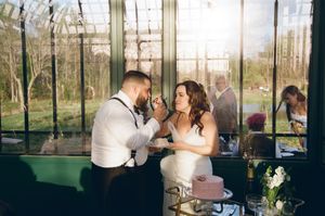 Wedding party members gather at the reception, seated at tables in an elegant glass-enclosed conservatory setting.