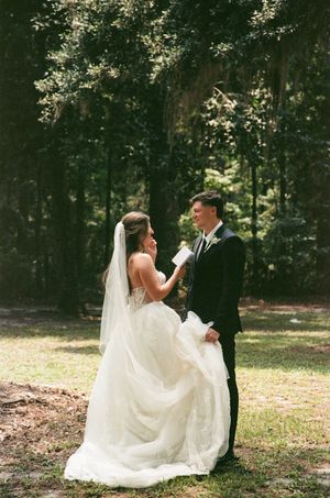 A wedding couple sits on the ground in a sunlit wooded area for a romantic photoshoot.