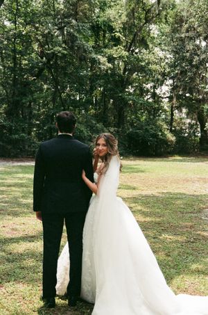 A bride in a flowing white gown embraces her partner during an outdoor woodland wedding photoshoot.